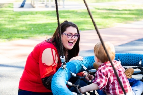 Mother pushing young son on swing at park - Australian Stock Image