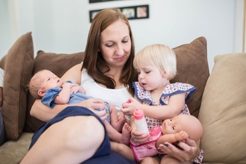 Mother sitting on lounge nursing newborn baby son while playing with daughter - Australian Stock Image