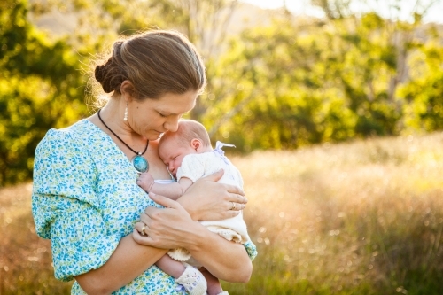 Mother snuggling her new daughter outside in sunlight - Australian Stock Image