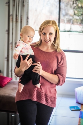 Mother standing holding baby in front of window - Australian Stock Image