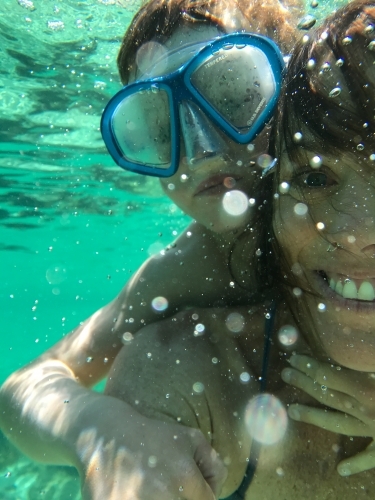 Mother with son on her back both wearing a snorkeling mask underwater - Australian Stock Image