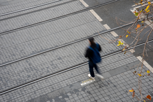 Motion blurred pedestrian crossing tram tracks seen from above - Australian Stock Image