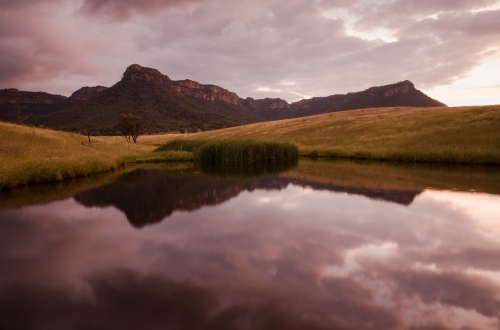 Mountain escarpment and sunset clouds reflected in farm dam - Australian Stock Image