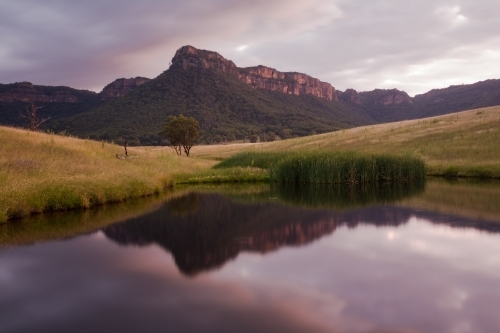 Mountain, paddock and sky reflected in farm dam water at sunset - Australian Stock Image