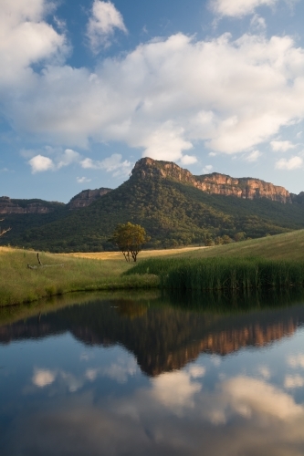 Mountain, paddock, sky and clouds reflected in farm dam water - Australian Stock Image