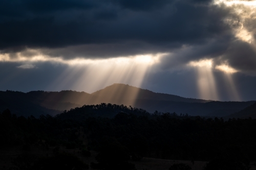 Mountains with sun rays piercing clouds at sunset - Australian Stock Image