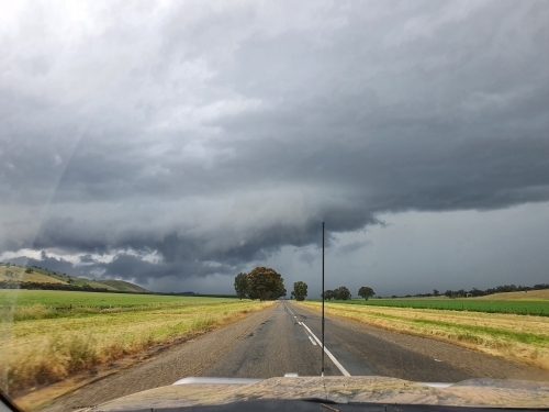 muddy vehicle on country road with stormy skies - Australian Stock Image