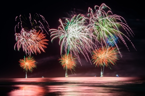 Multi coloured fireworks exploding over an ocean in the night sky. - Australian Stock Image