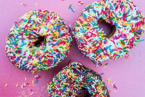 multi coloured sprinkles on donut, on pink background - Australian Stock Image