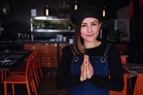 Multicultural Asian small business owner greeting in front of Thai restaurant - Australian Stock Image