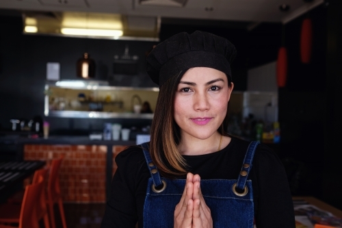 Multicultural Asian small business owner greeting in front of Thai restaurant - Australian Stock Image