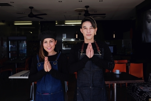 Multicultural Asian small business owners greeting in front of Thai restaurant - Australian Stock Image