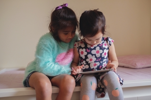 Multicultural kids using tablet in bedroom - Australian Stock Image