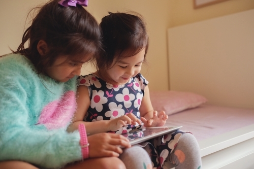 Multicultural kids using tablet in bedroom - Australian Stock Image