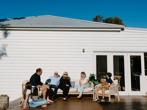 Multigeneration family sitting outside the wooden deck in the garden. - Australian Stock Image