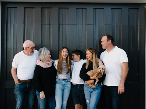 Multigenerational family standing outside in front of black garage door - Australian Stock Image