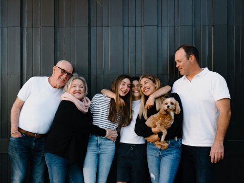 Multigenerational family standing outside in front of black garage door - Australian Stock Image