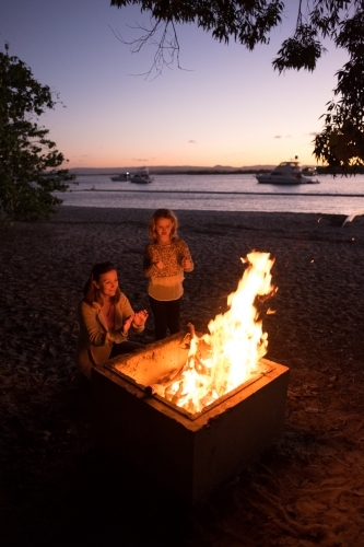 Mum and daughter sitting around camp fire - Australian Stock Image