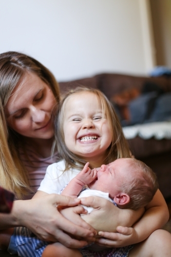 Mum holds her excited daughter and newborn son on her lap - Australian Stock Image