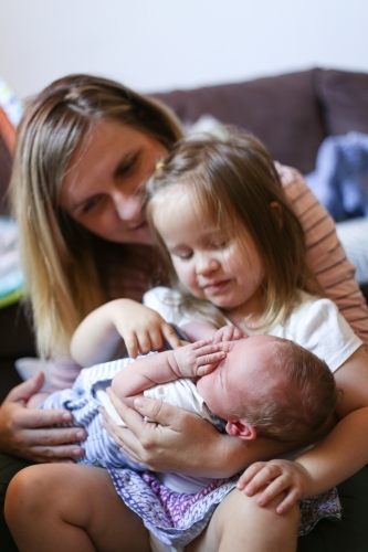 Mum holds her toddler daughter and newborn son on her lap - Australian Stock Image