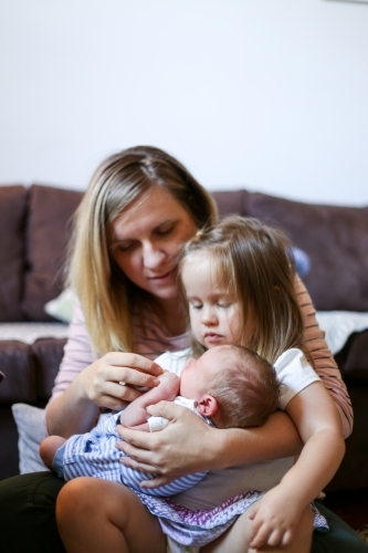 Mum holds her toddler daughter and newborn son on her lap - Australian Stock Image