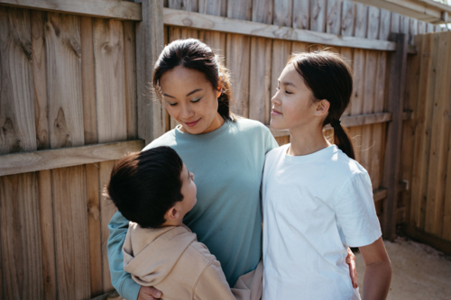 Mum hugging her children outside their house. - Australian Stock Image