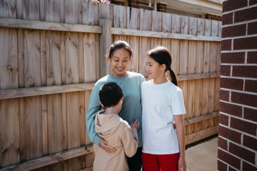 Mum hugging her children outside their house. - Australian Stock Image