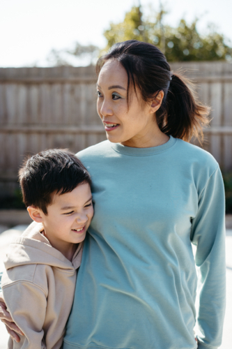 Mum hugging her son in their yard. - Australian Stock Image