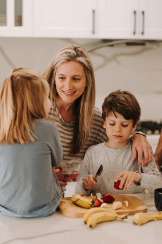 mum teaching kids how to cut fruit in the kitchen - Australian Stock Image