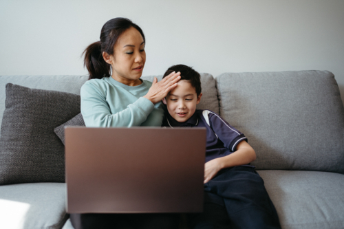 Mum working on her laptop on the couch with her kids. - Australian Stock Image