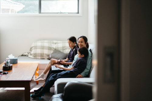 Mum working on her laptop on the couch with her kids. - Australian Stock Image