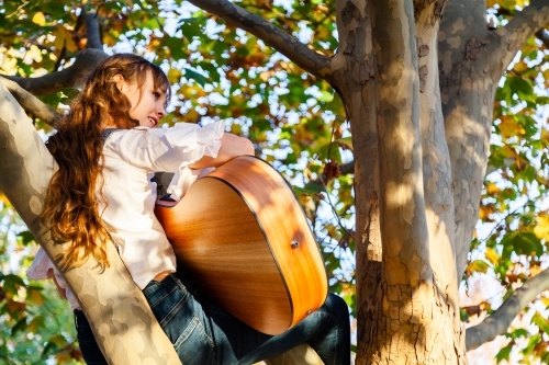 Musician sitting in a tree dreaming with guitar - Australian Stock Image
