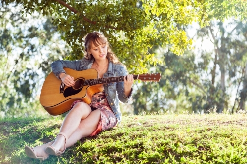 Musician sitting on a hill outside playing guitar - Australian Stock Image