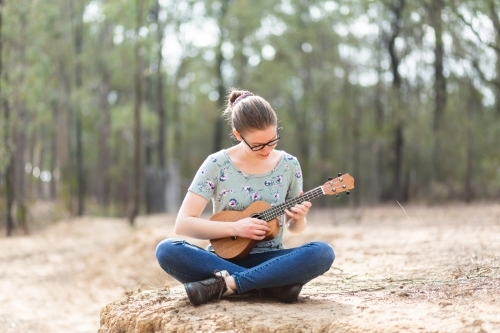 Musician with ukulele playing instrument in dry paddock - Australian Stock Image