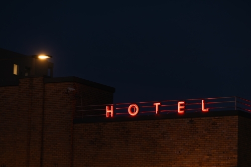 Neon Hotel sign illuminated on top of building at night time - Australian Stock Image