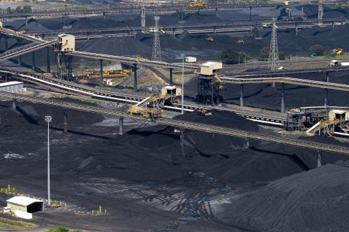 network of conveyor belts over coal terminal heaps with bulldozers and trains in the background. - Australian Stock Image