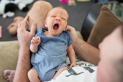 Newborn baby boy lying in father's lap yawning - Australian Stock Image