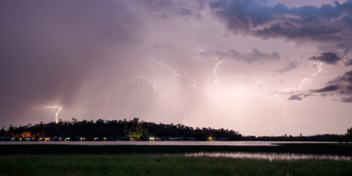 Night time lightning storm over lake and cabins - Australian Stock Image