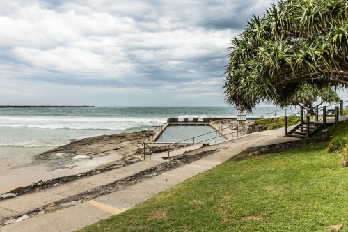 Ocean pool next to walking path and tree at beach with ocean waves - Australian Stock Image