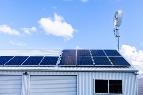 off grid sustainable living with solar panels and wind turbine on shed roof - Australian Stock Image