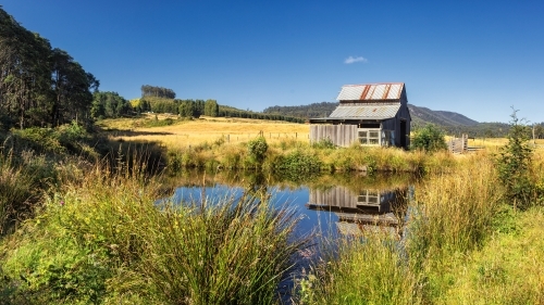 Old farm building reflected in pond. - Australian Stock Image