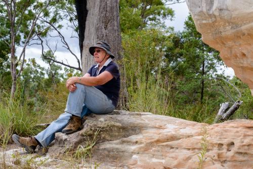 Old woman sitting on rock in remote, rugged setting - Australian Stock Image