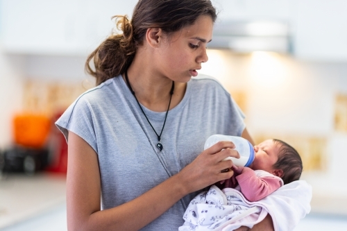 older girl bottle feeding her newborn baby sister - Australian Stock Image