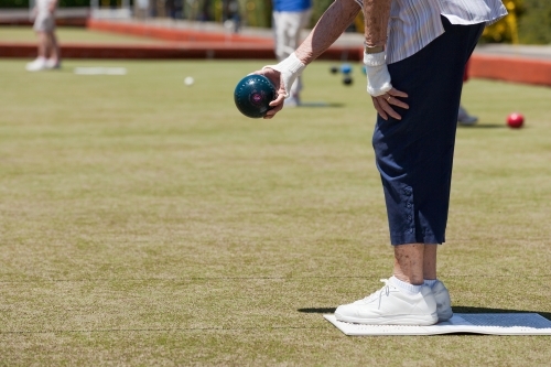 Older woman lining up at shot at lawn bowls - Australian Stock Image