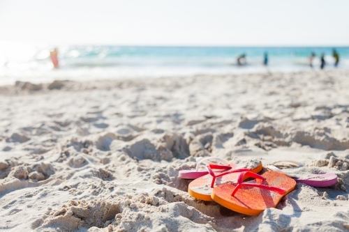 Orange and pink thongs left on sand at busy beach - Australian Stock Image