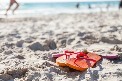 Orange and pink thongs left on sand at busy beach - Australian Stock Image