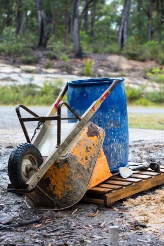 Orange wheelbarrow and blue barrel on wooden pallet - Australian Stock Image