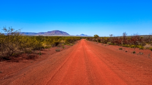 Outback red dirt road leading to mountains and blue sky