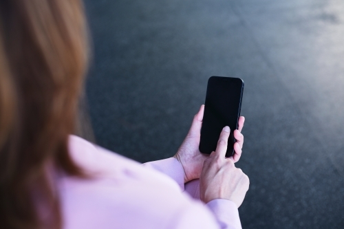 Over the shoulder shot of woman typing on mobile phone - Australian Stock Image