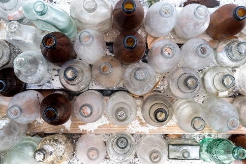 overhead shot of empty uncapped bottles on wooden plank with white sand scattered all over it - Australian Stock Image